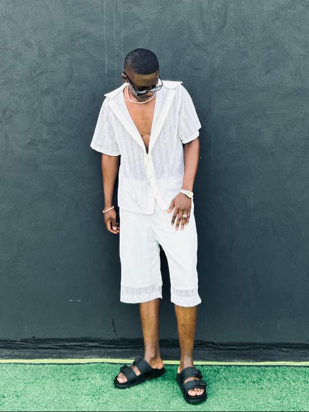 Person wearing a white outfit standing against a textured dark green wall.
